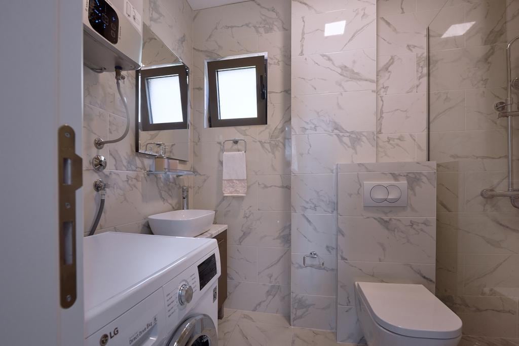 Modern bathroom with marble-effect finishes, a walk-in shower, and a washing machine in an apartment, Pržno, Montenegro.