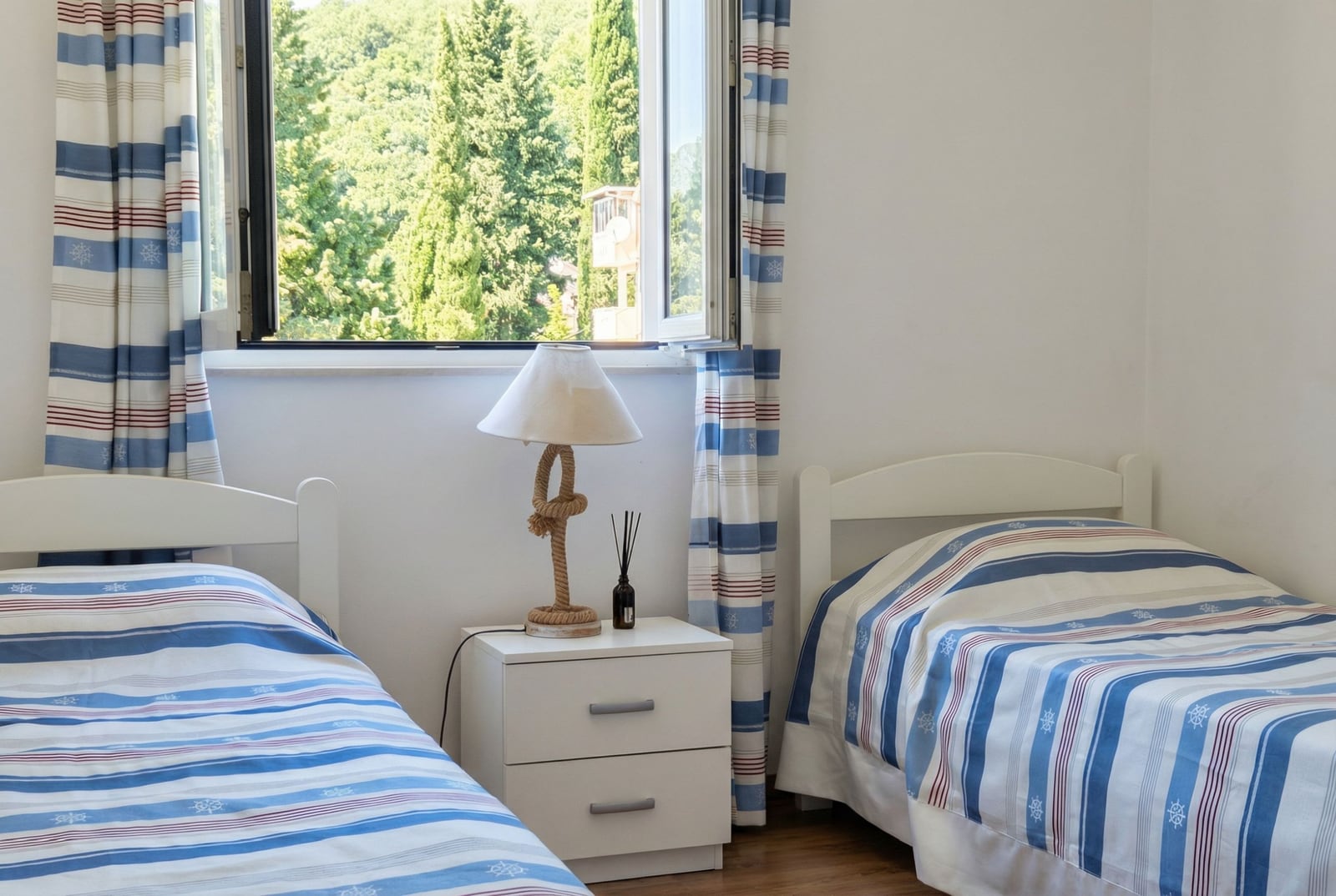 Bedroom with two beds, nautical decor, and a view of greenery in an apartment in Tivat, Montenegro.
