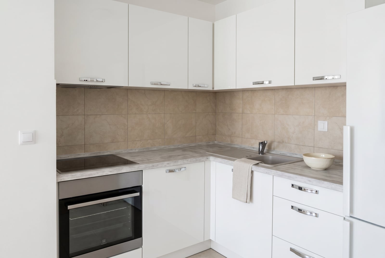 Modern white kitchen in a Budva, Montenegro apartment: built-in appliances, light-colored countertop, and tiled backsplash.