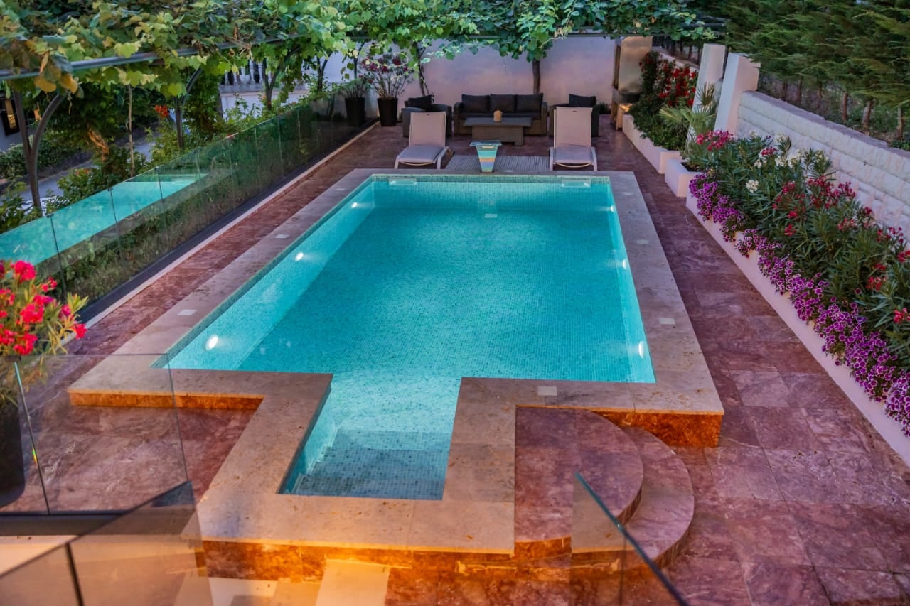 Private pool with lighting and a relaxation area at a villa in Budva, Montenegro: sun loungers, terrace, and a blooming garden.