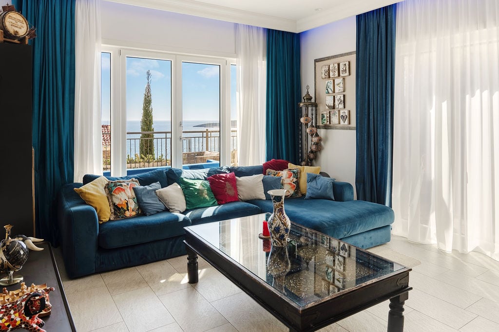 Living room in a Luštica townhouse, Montenegro: blue sofa, glass coffee table, and panoramic sea view from the window.