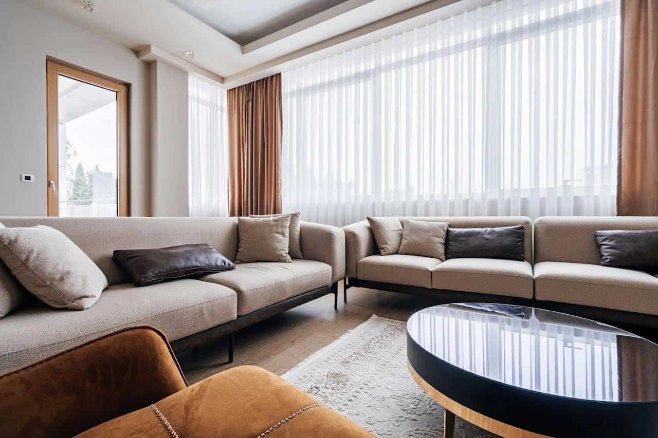 Modern living room in an apartment in Budva, Montenegro: beige sofas, panoramic windows, and a round coffee table.