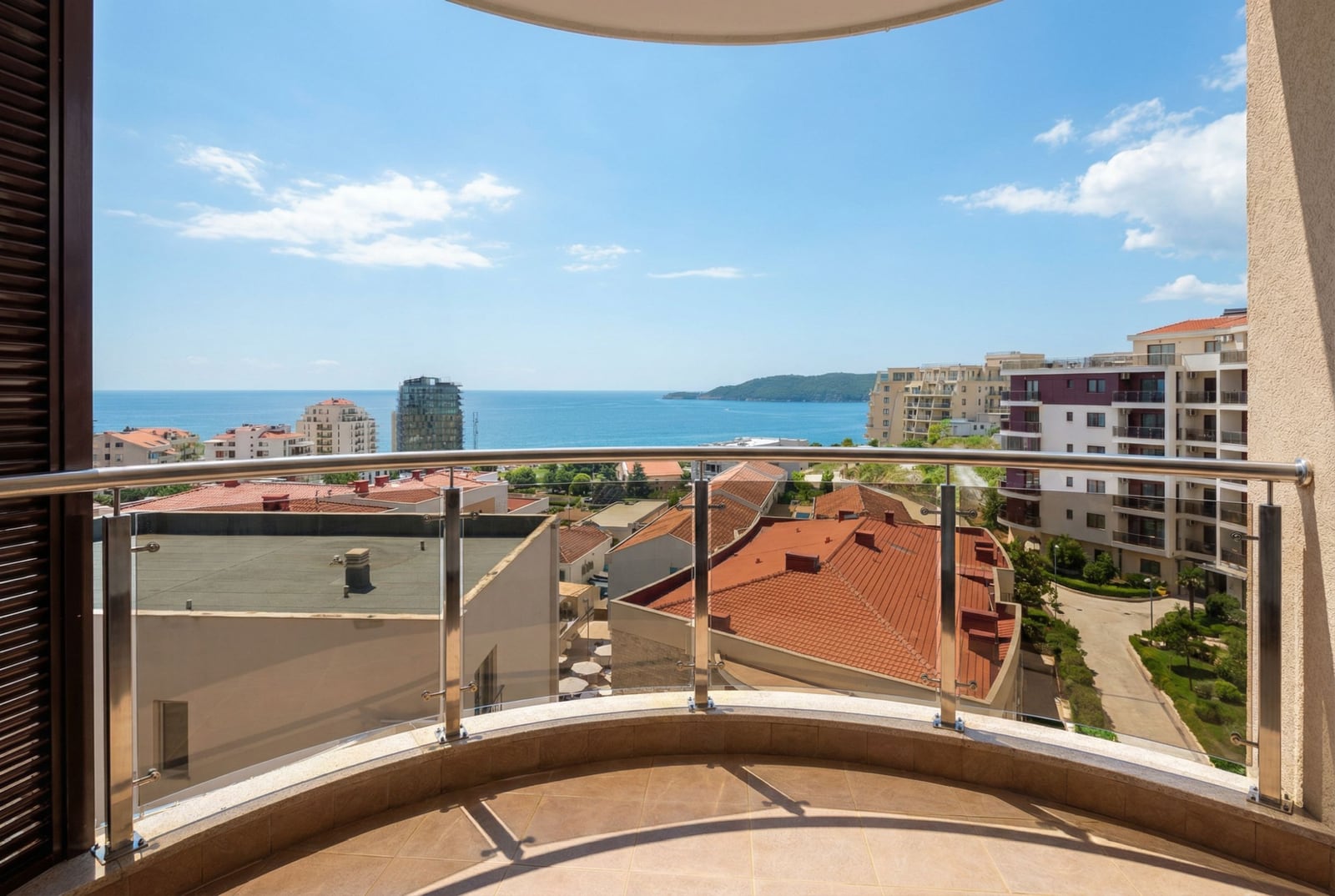 View from the apartment balcony in Bečići, Montenegro: panoramic sea view, tiled rooftops, and modern architecture.