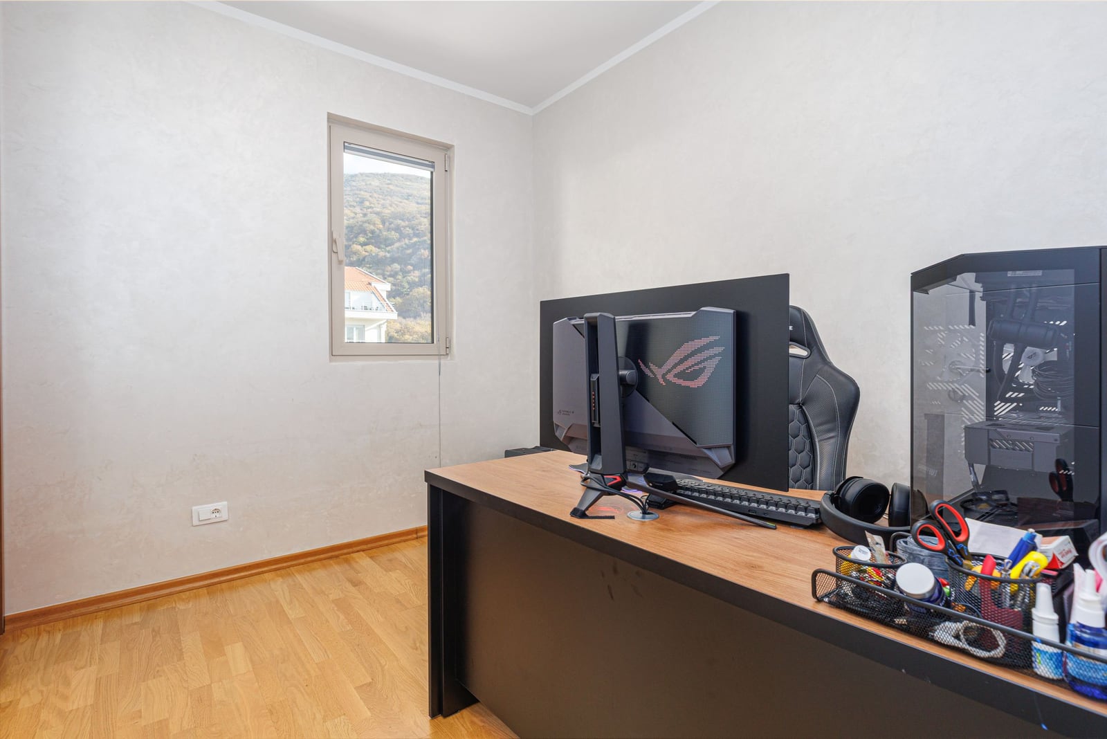 Home office in a penthouse in Bečići, Montenegro: computer desk, gaming chair, and mountain view from the window.