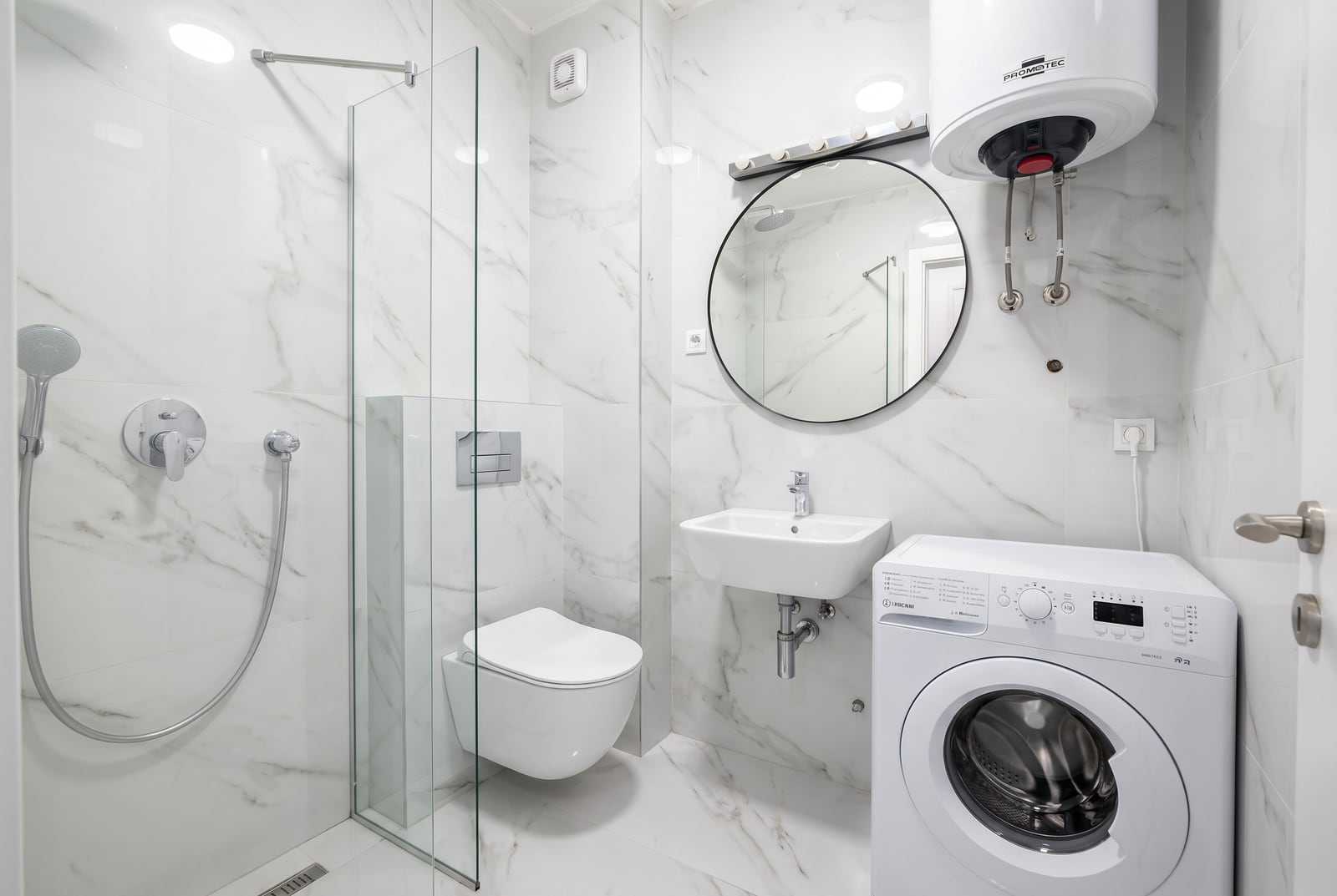 Modern bathroom with marble tiles, glass shower enclosure, wall-mounted toilet, sink, and washing machine.