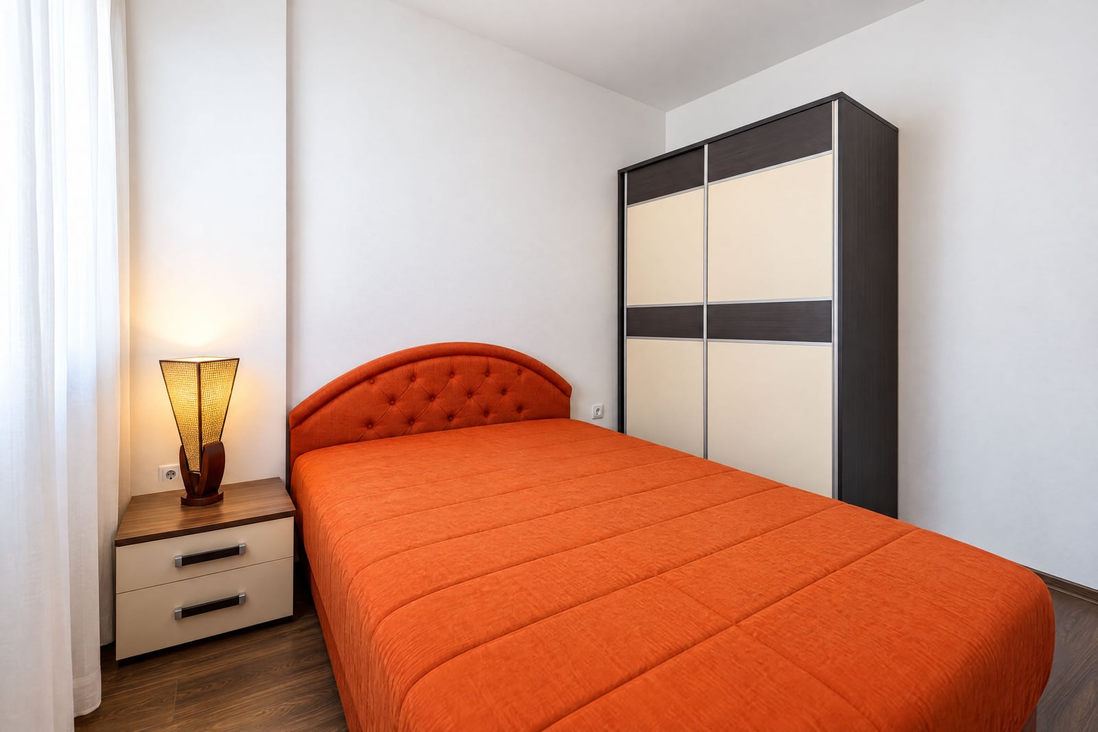 Bedroom featuring an orange bed, a nightstand with a lamp, and a sliding door wardrobe on wood flooring.