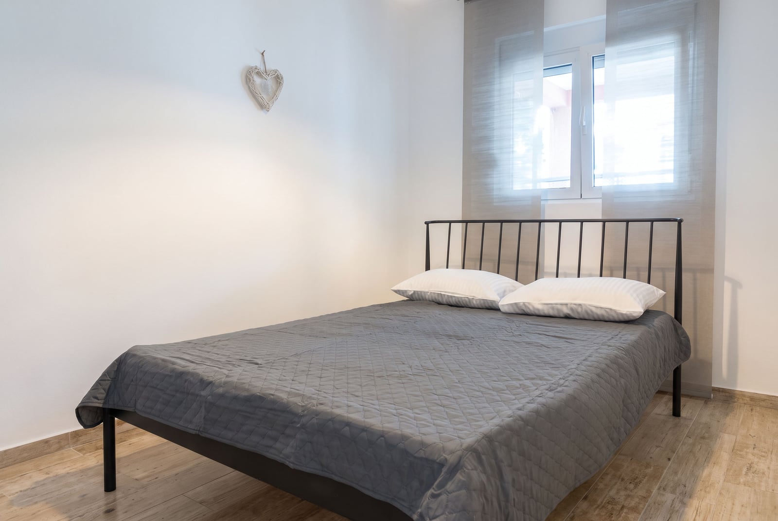 Bedroom featuring a black metal bed frame, gray quilted cover, white pillows, and wood flooring.