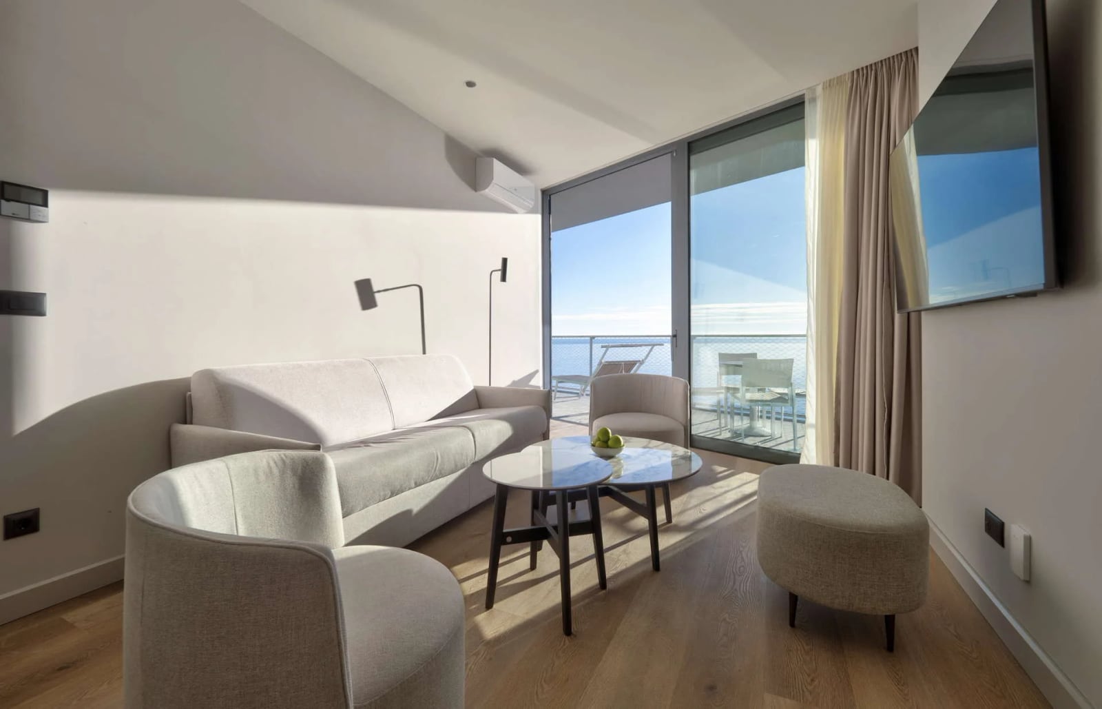 Bright room with a sofa, armchairs, and coffee table facing a large window overlooking the sea.