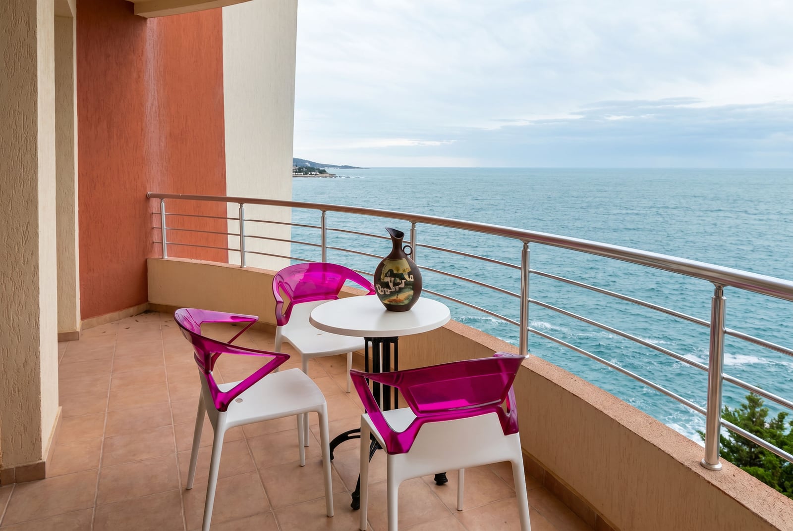 Balcony with a sea view in an apartment in Bar, Montenegro: a table and modern pink chairs on the terrace.