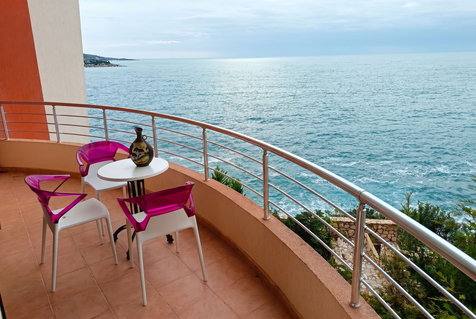 Balcony with a sea view in an apartment, Bar, Montenegro: a table and pink chairs on a terrace with a panoramic view.