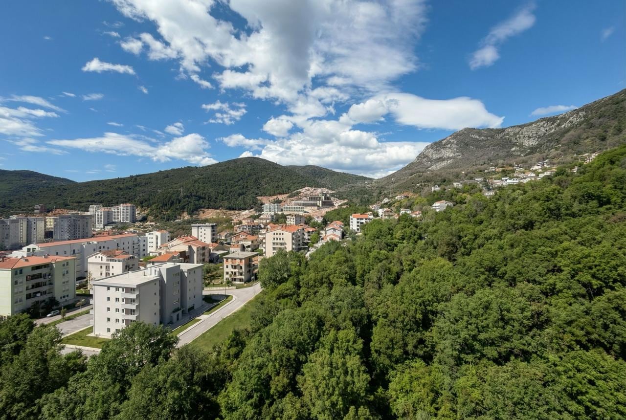 Panoramic view of the Budva residential area, Montenegro: modern houses, green hills, and mountains against a blue sky.