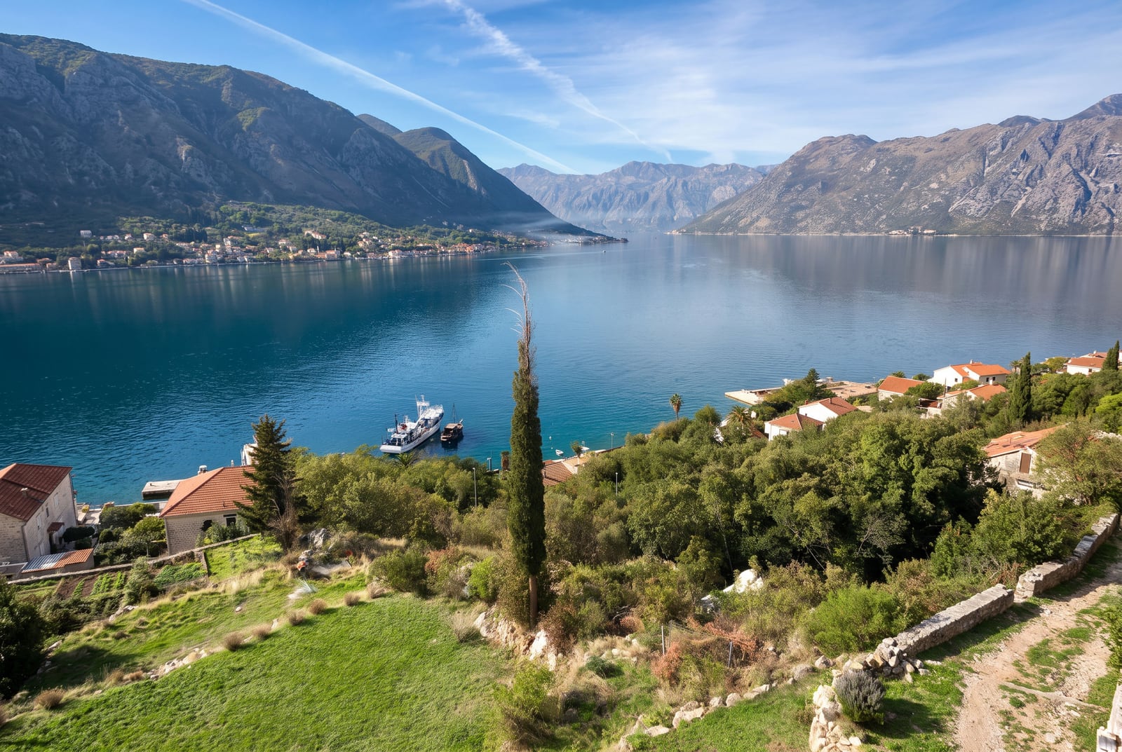 Panoramic view of a bay surrounded by mountains, with houses and a boat near the shore.