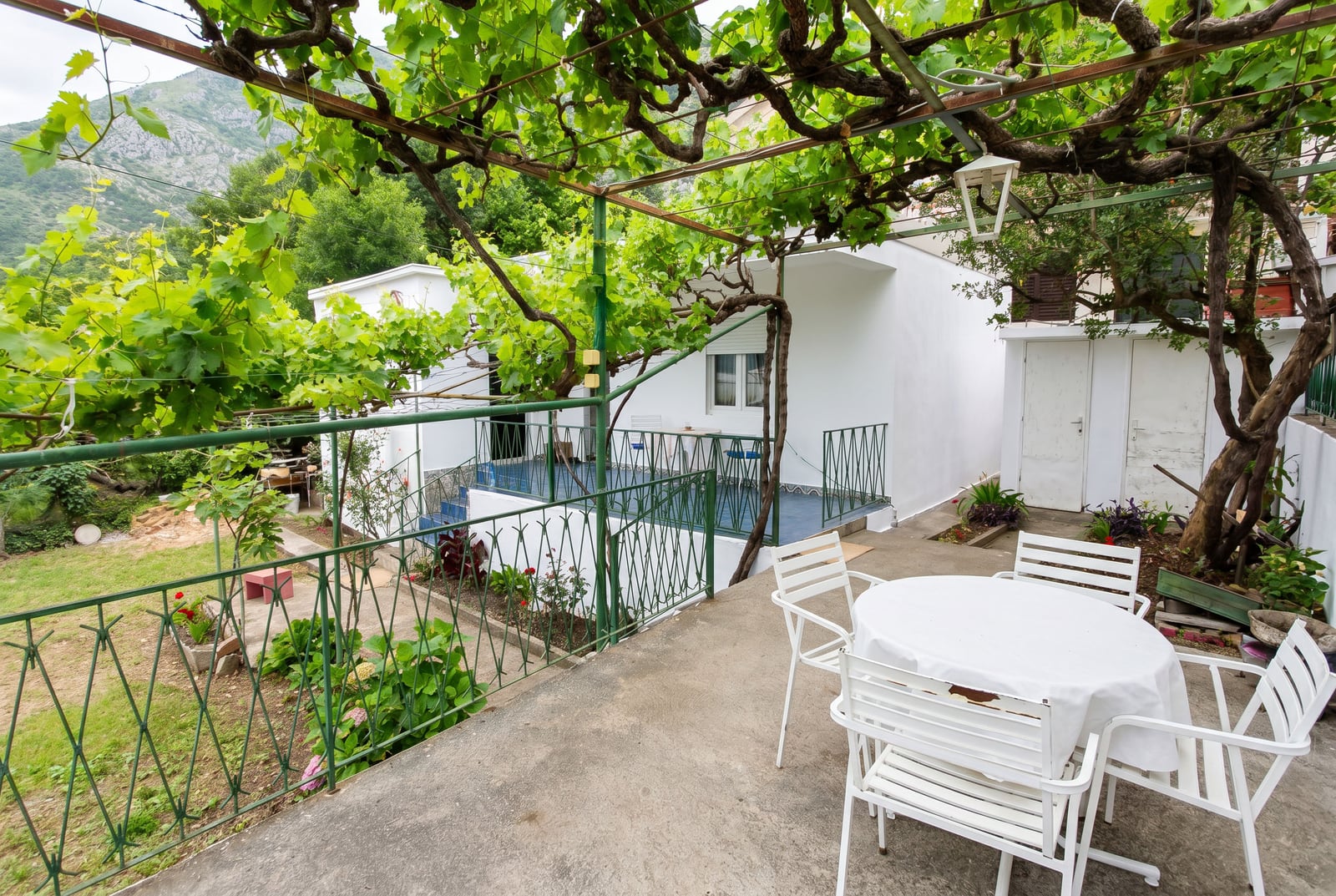 Cozy terrace with white furniture and a grapevine pergola at a house in Sutomore, Montenegro, with a view of the garden and mountains.