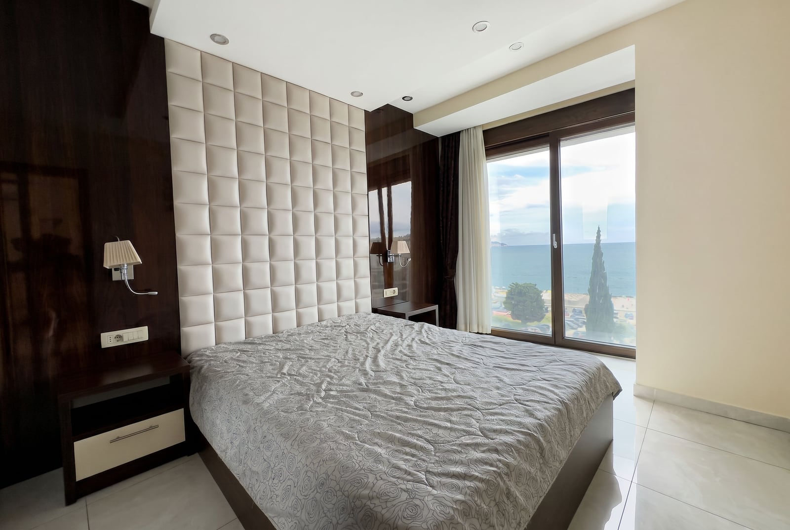 Bedroom in an apartment in Bečići, Montenegro: double bed with a soft headboard and a panoramic sea view from the window.