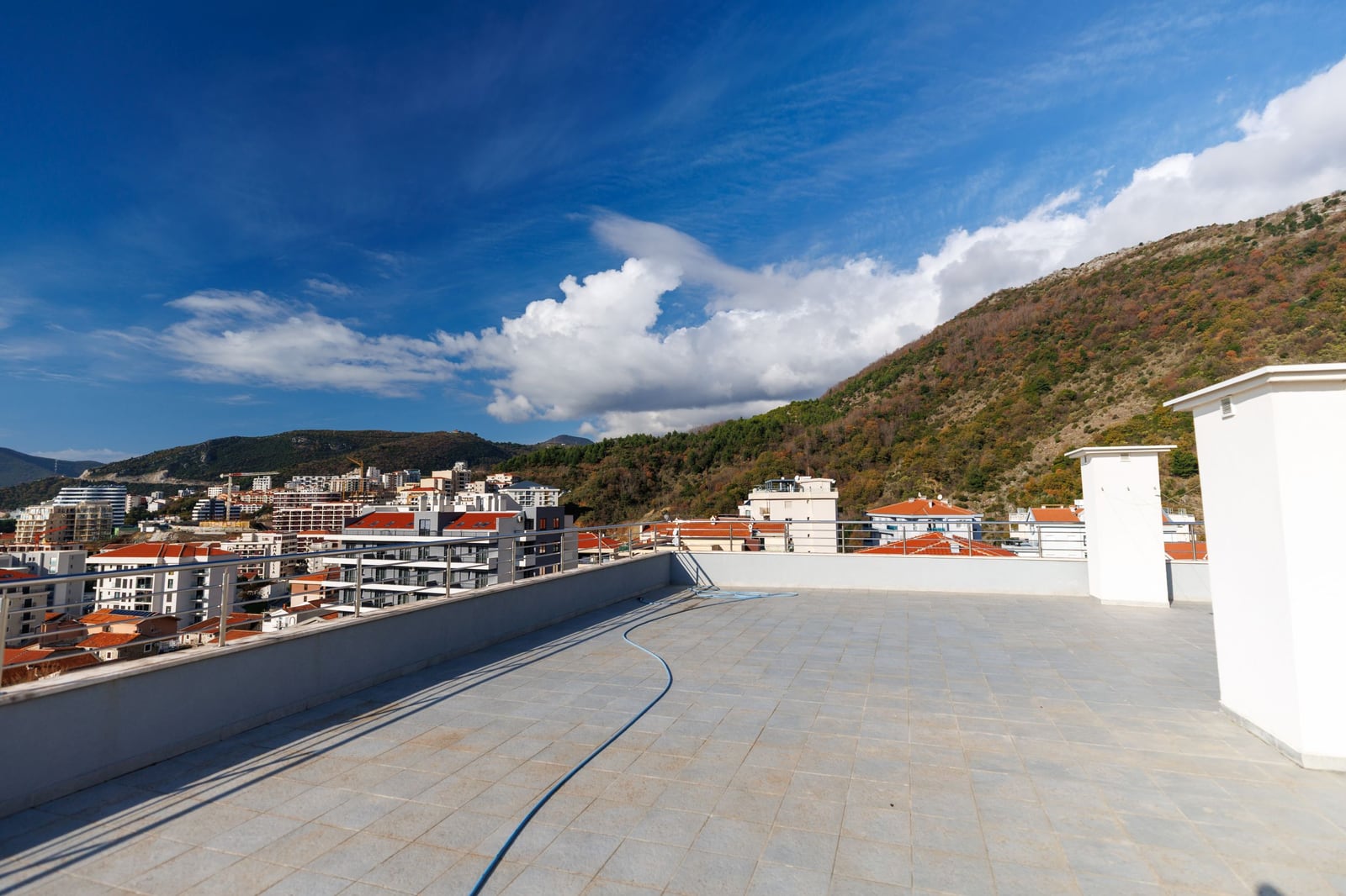 Spacious open penthouse terrace in Becici, Montenegro, with panoramic views of the mountains and the cityscape.