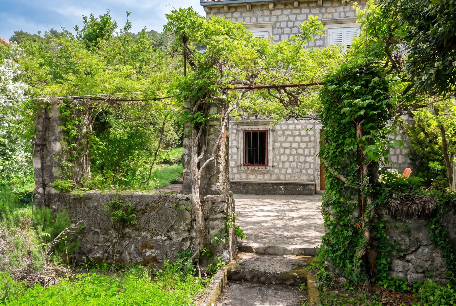 Stone house in Dobrota, Montenegro: cozy courtyard with a vine-covered terrace and traditional stone facade.