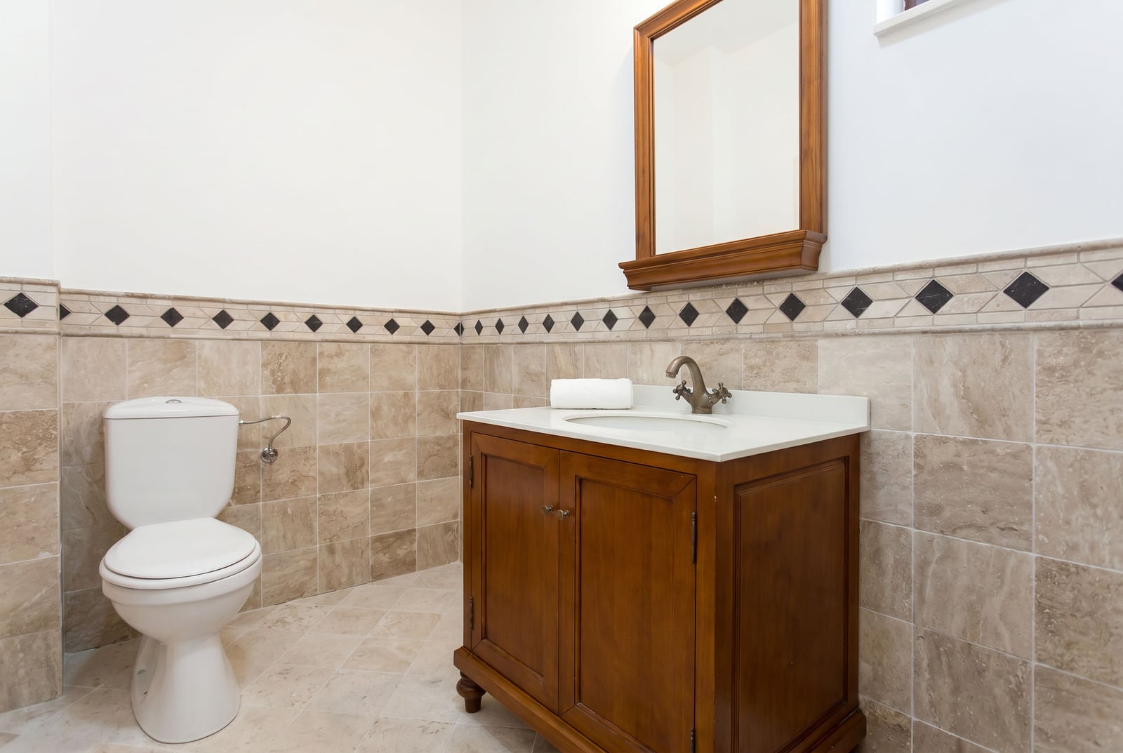 Bathroom in an apartment in Risan, Montenegro: classic wooden vanity, mirror, and beige tiles with decorative accents.