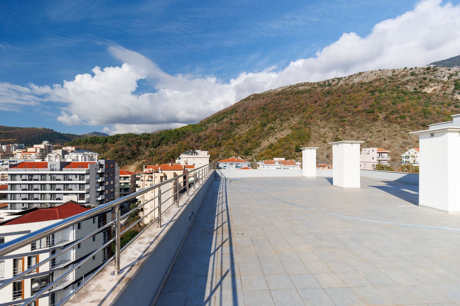 Open penthouse terrace in Becici, Montenegro, with views of the mountains and urban landscape, paved with light-colored tiles.