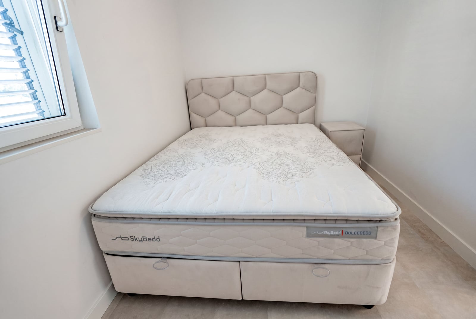 Double bed with an upholstered headboard in a bright bedroom of an apartment in Sveti Stefan, Montenegro.