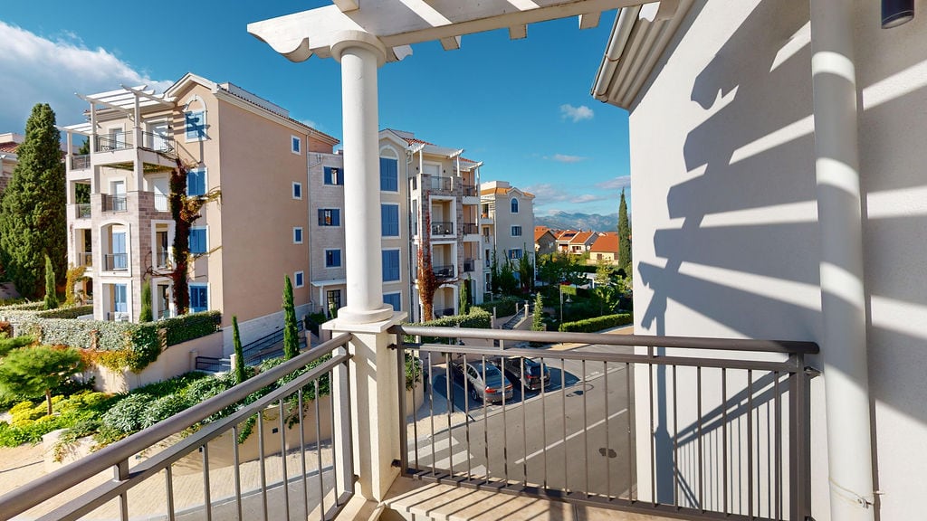 View from the balcony overlooking the residential complex in Luštica, Montenegro: a terrace with a pergola, modern architecture, and a green courtyard.