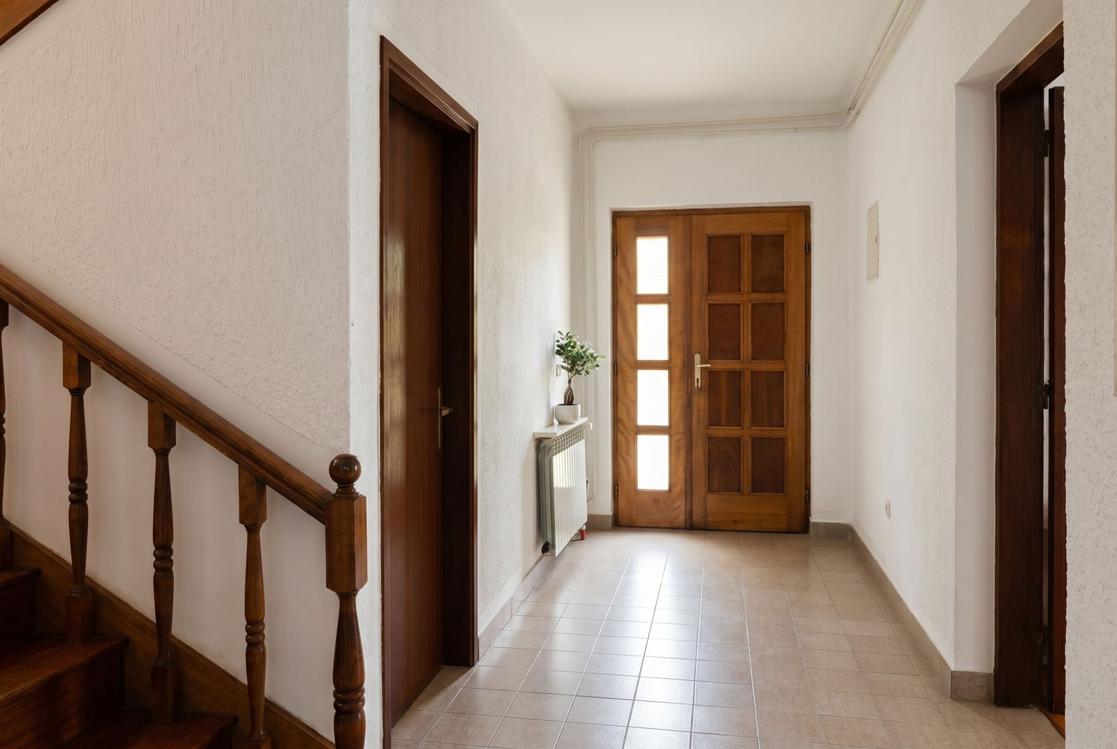 Bright hallway with a wooden staircase and doors in a house, Lastva, Montenegro. Tiled floor and classic interior.