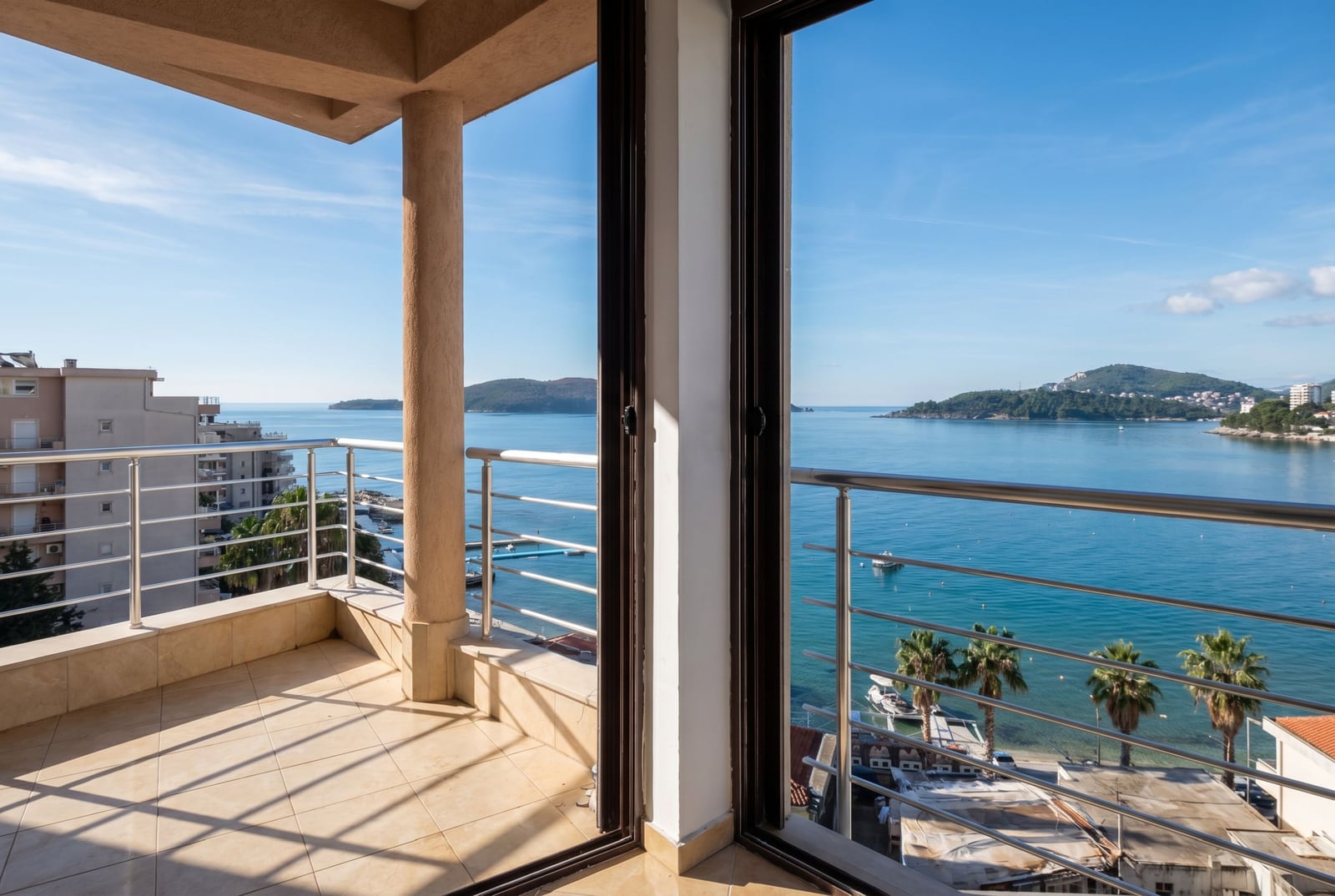 Spacious balcony with panoramic sea and beach views in an apartment, Rafailovici, Montenegro: tile flooring and metal railings.