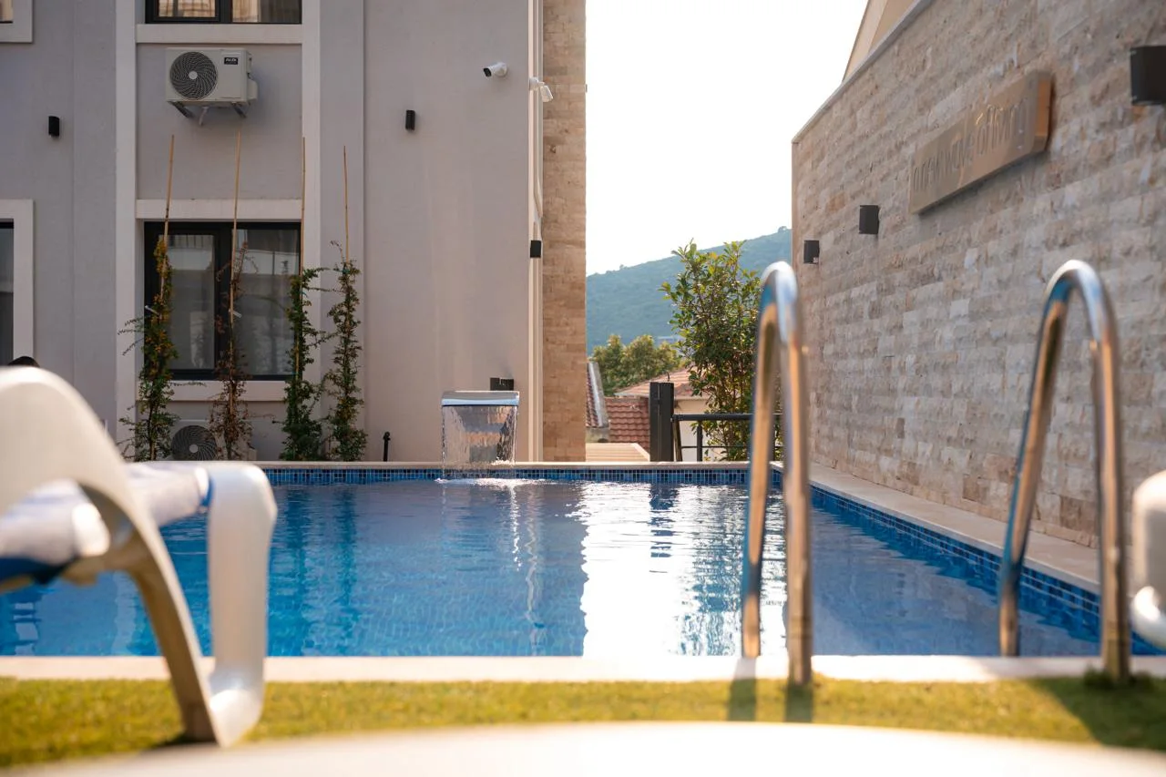 Outdoor swimming pool with blue water, metal ladders, and a white lounge chair against a stone wall.