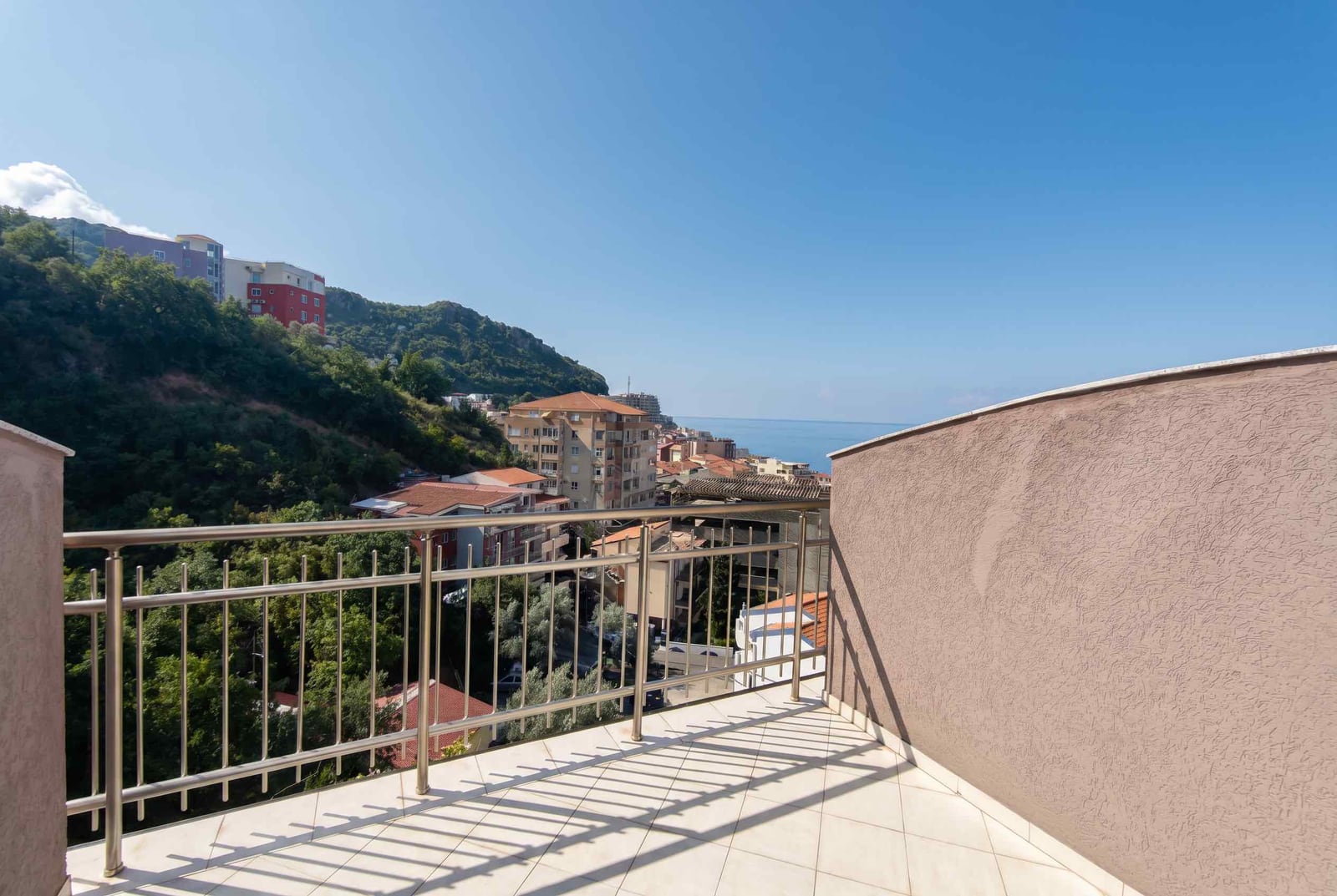 Open balcony with a view of the sea and mountains in an apartment, Bečići, Montenegro. Light-colored tiles and metal railings.