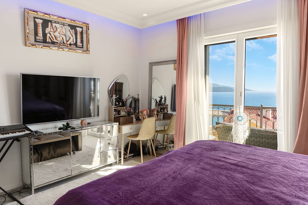 Bedroom in a Luštica Bay townhouse, Montenegro: bed with a purple bedspread, mirrored nightstand, and sea view.