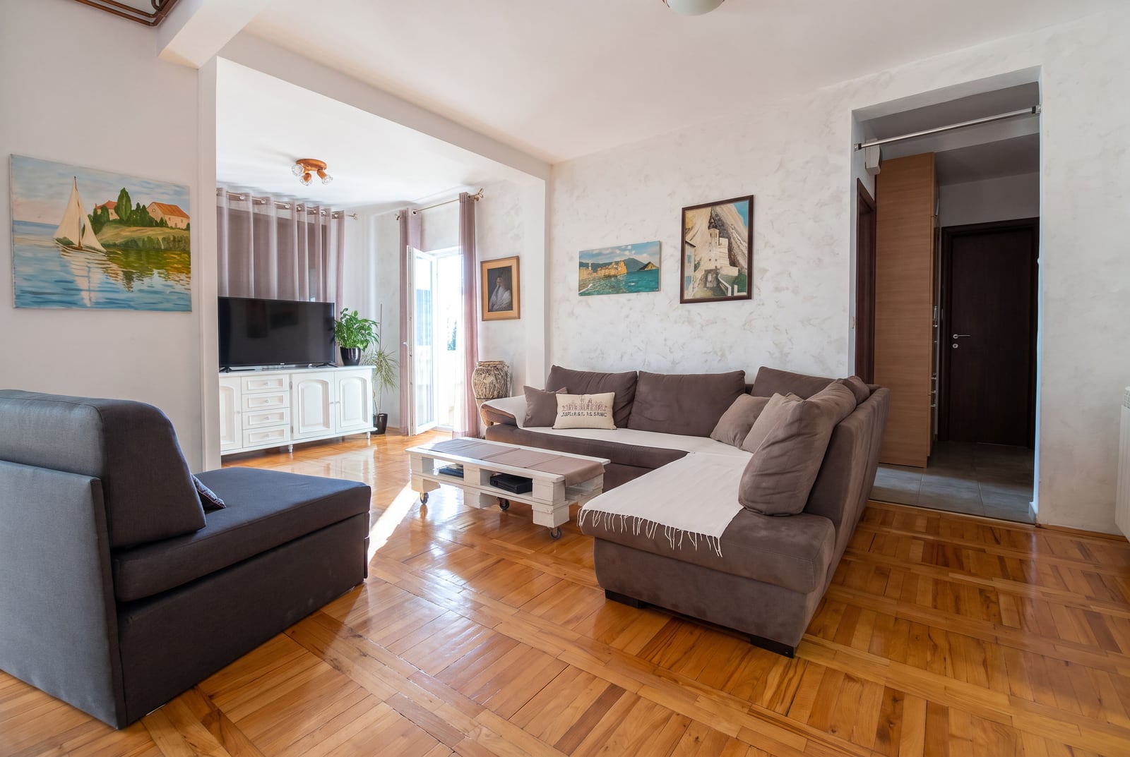 Living room with a large brown sectional sofa, wooden parquet floor, and TV unit.
