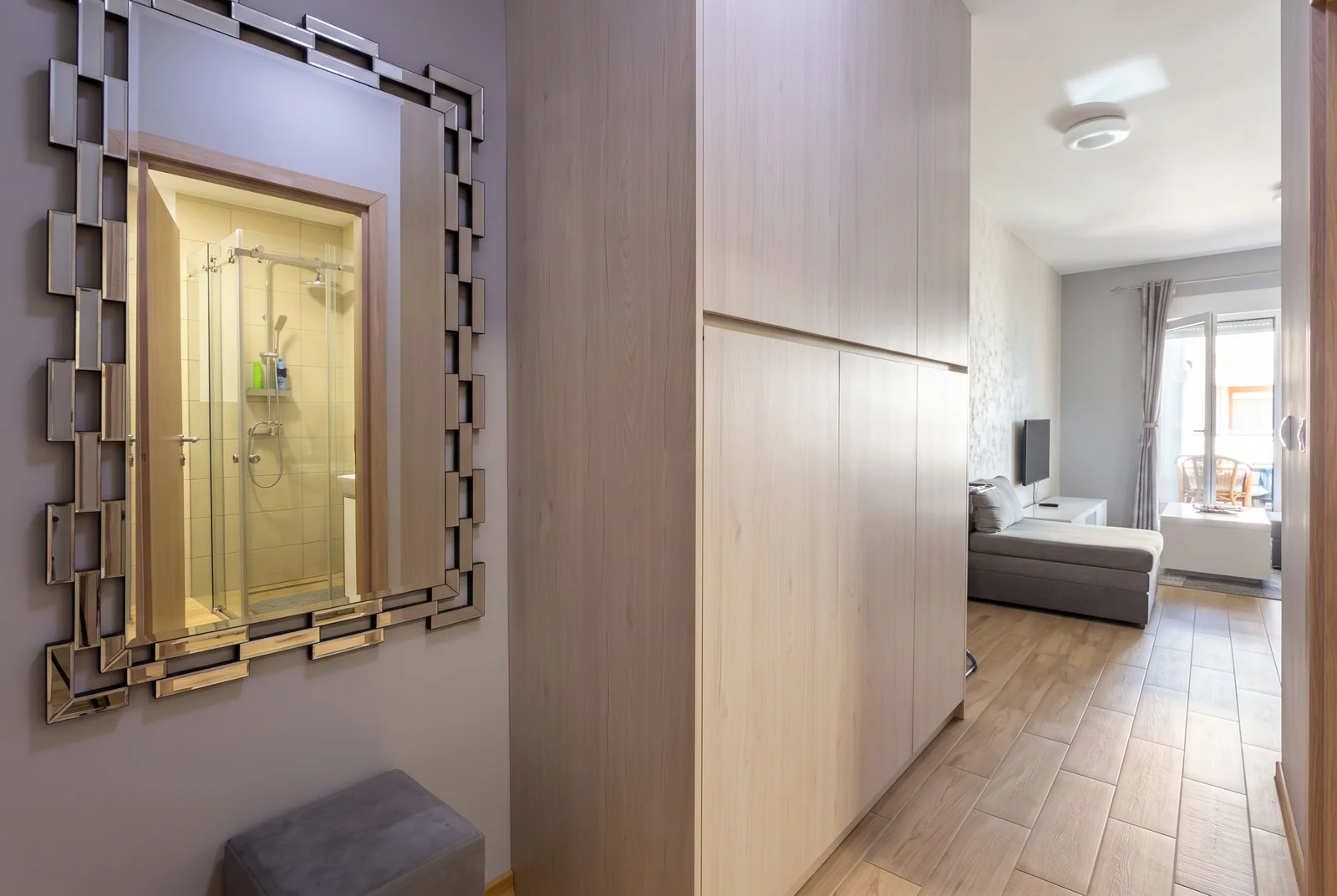Hallway with a large mirror reflecting a shower, a wooden wardrobe, and a view into the living room.