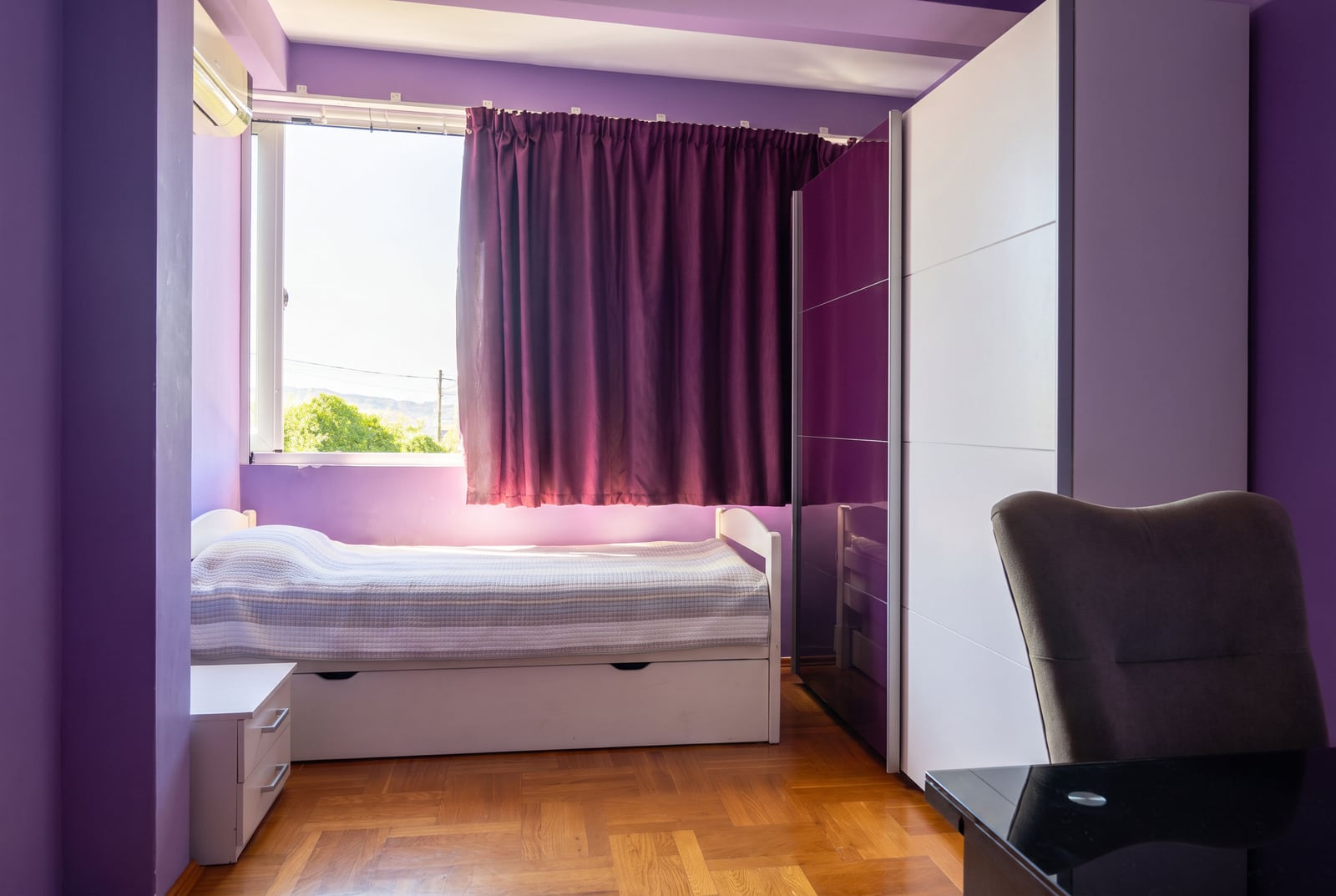 Bedroom with purple walls, a single bed with storage, a wardrobe, and wooden parquet flooring.