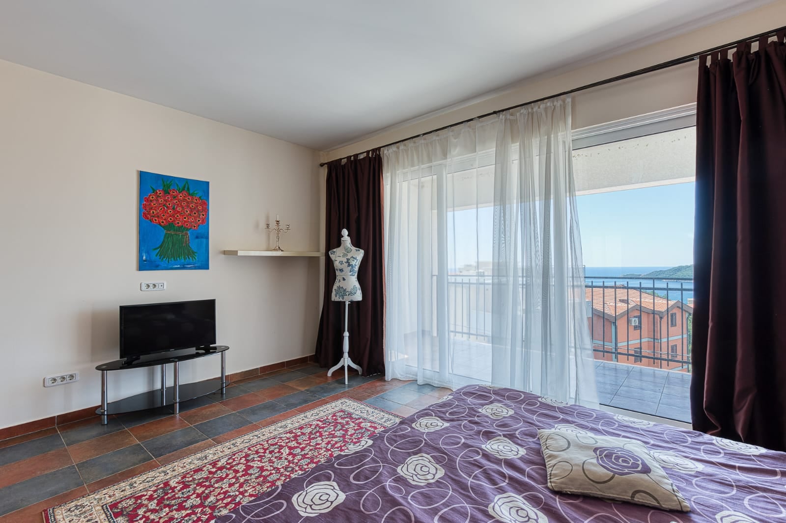 Bedroom in a villa in Becici, Montenegro: bed, TV, mannequin, and panoramic balcony with a view of the sea and mountains.