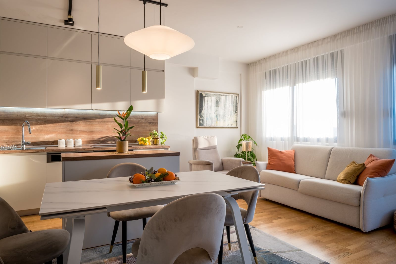 Modern living room with kitchen in a Tivat apartment, Montenegro: dining area, light-colored furniture, and panoramic window.