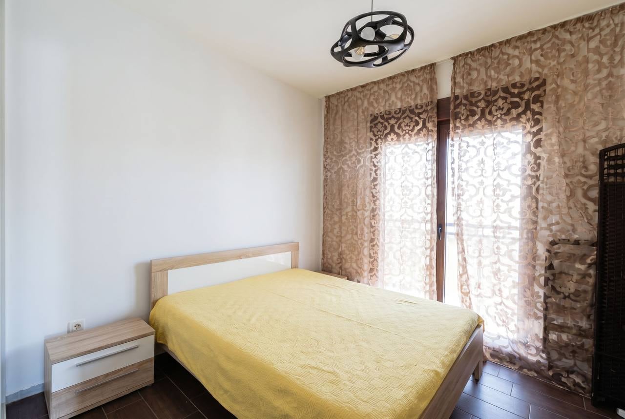 Cozy bedroom with a double bed in an apartment in Budva, Montenegro: light finishes, panoramic window with sheer curtains.
