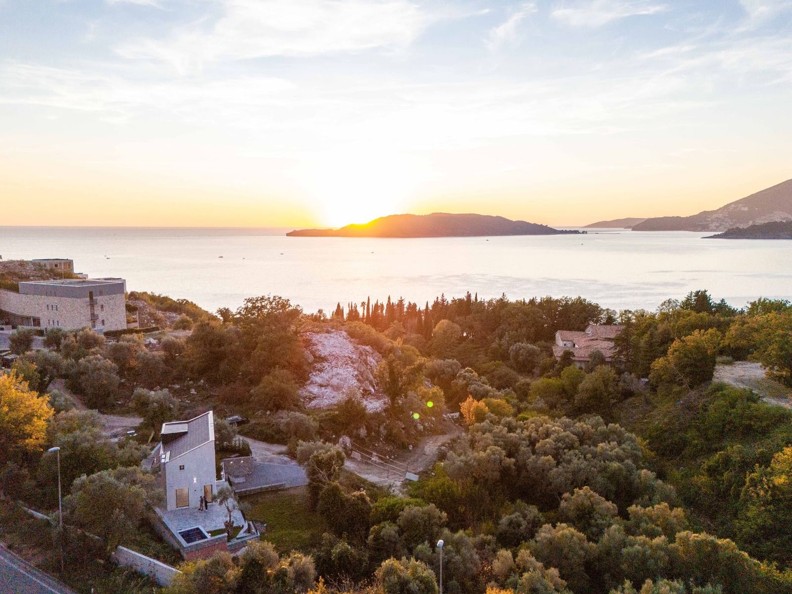 Modern villa in Kamenovo, Montenegro, with panoramic sea and island views at sunset, surrounded by greenery.