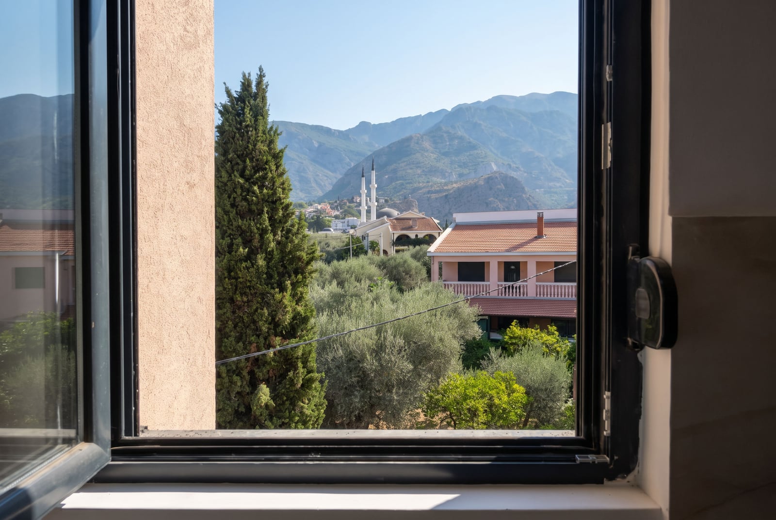 View from the apartment window in Bar, Montenegro: a panorama of green mountains, cypresses, and tiled rooftops.