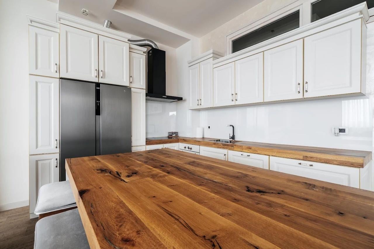 Modern kitchen in an apartment in Budva, Montenegro: white cabinets, natural wood countertop, and appliances.
