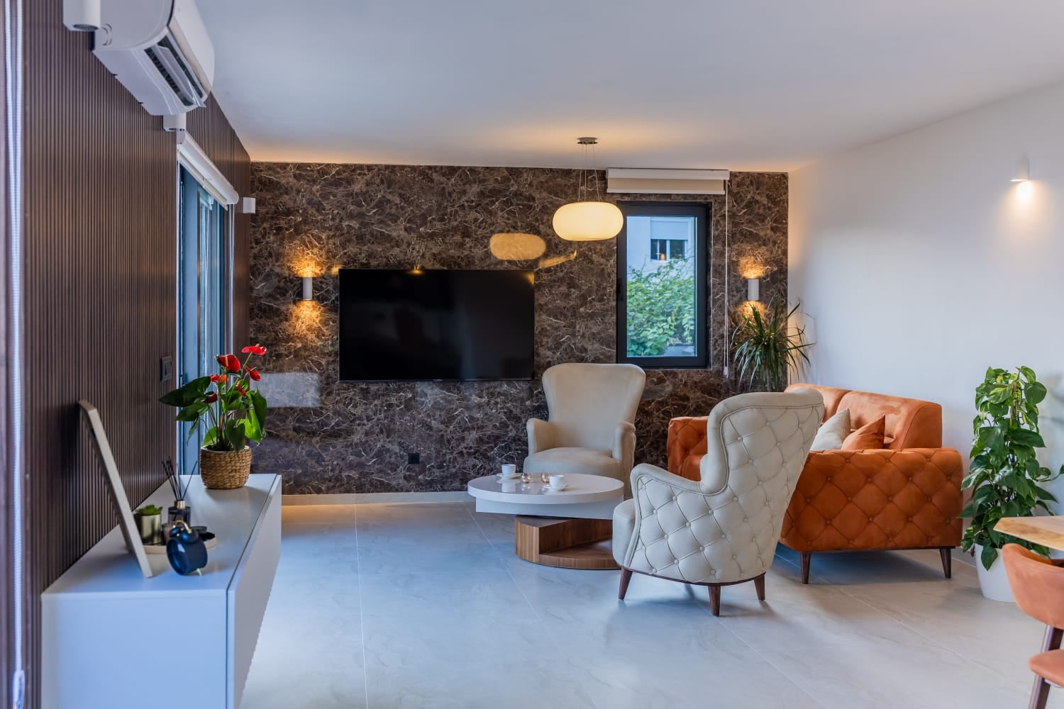 Modern living room with a marble wall and upholstered furniture in a villa in Budva, Montenegro. Interior with TV and armchairs.