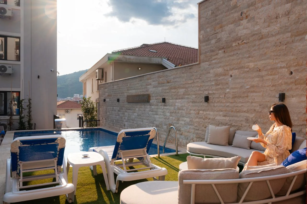 Outdoor area featuring a swimming pool, blue lounge chairs, and a sofa set on artificial grass next to a stone wall.