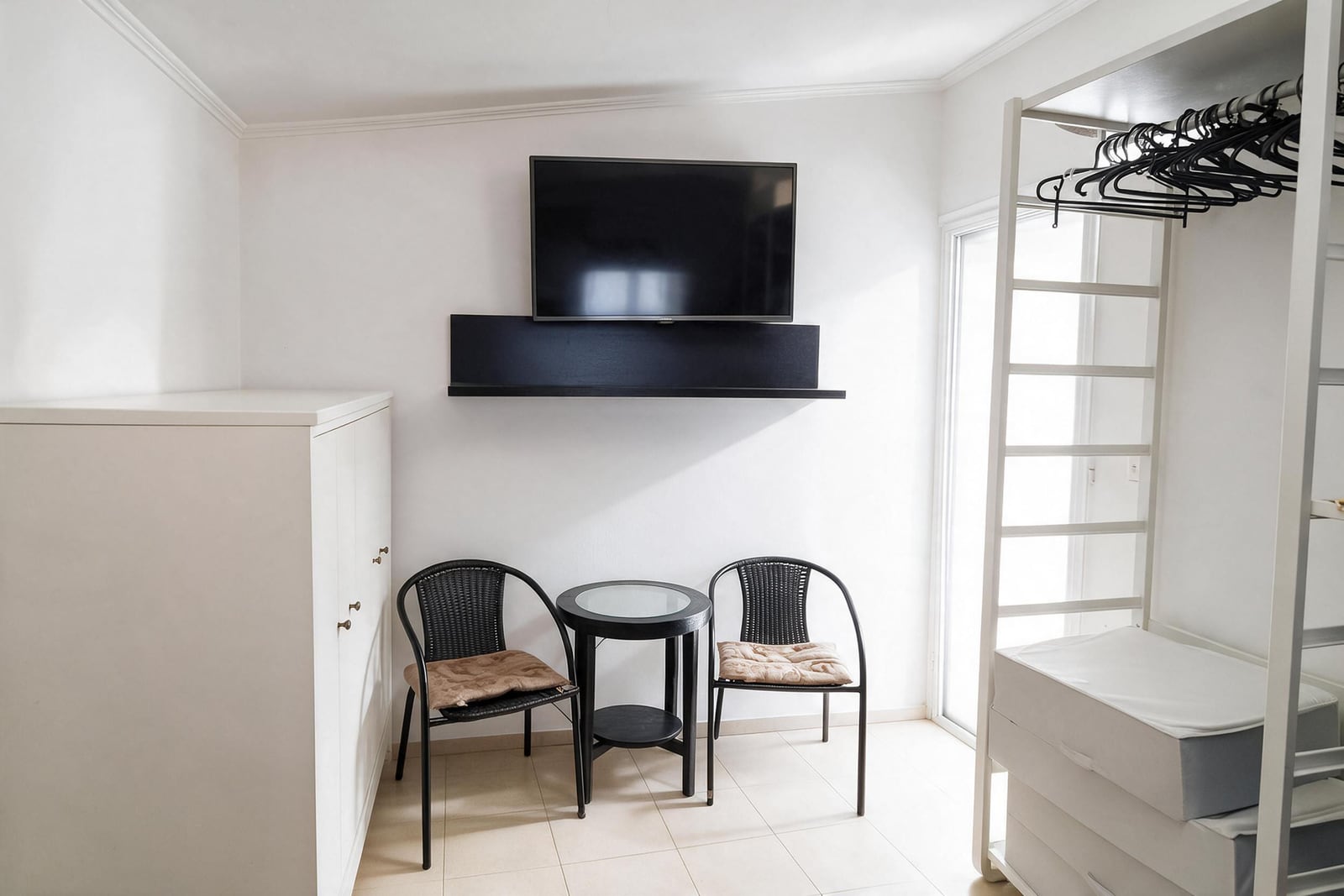 Small seating area with two black chairs, a table, and a wall-mounted TV next to an open wardrobe frame.