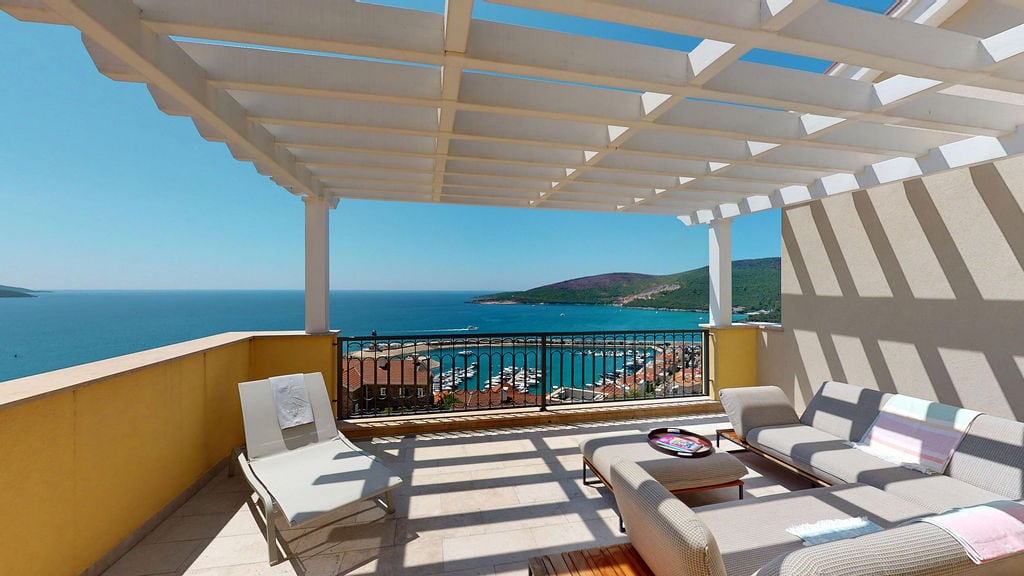 Terrace with a pergola and marina view in Luštica, Montenegro: soft furniture, sun lounger, and panoramic sea view.