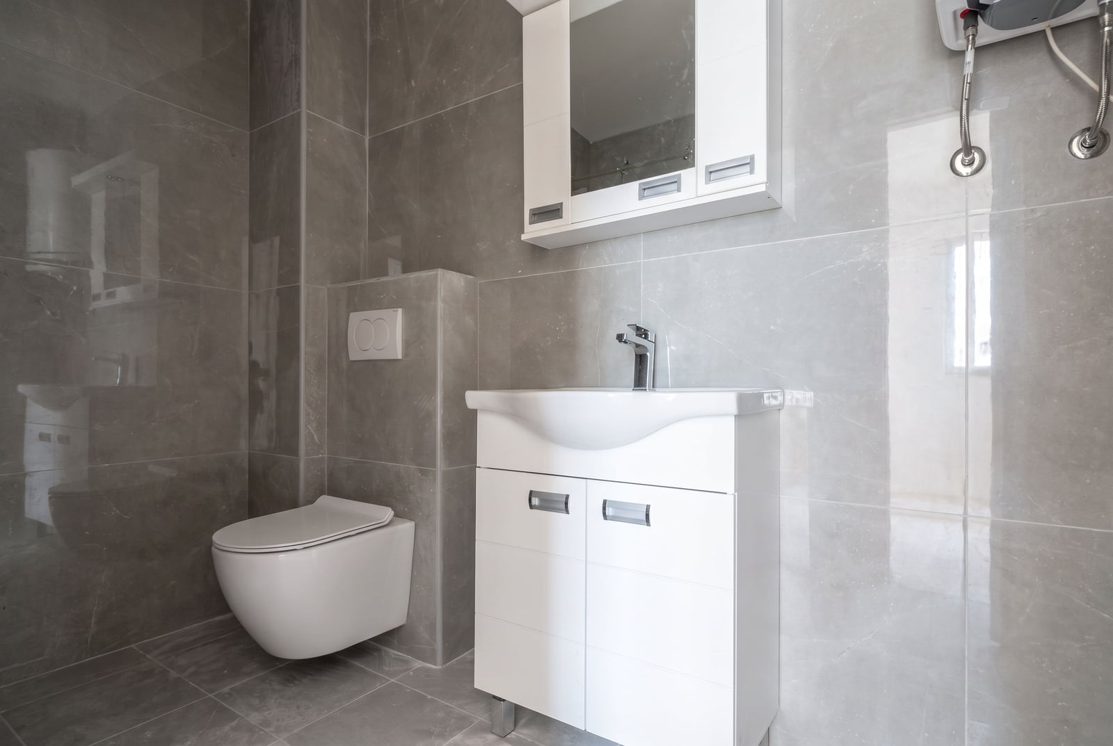 Modern bathroom with gray tiles, white vanity, sink, and wall-hung toilet in an apartment in the city of Bar, Montenegro.