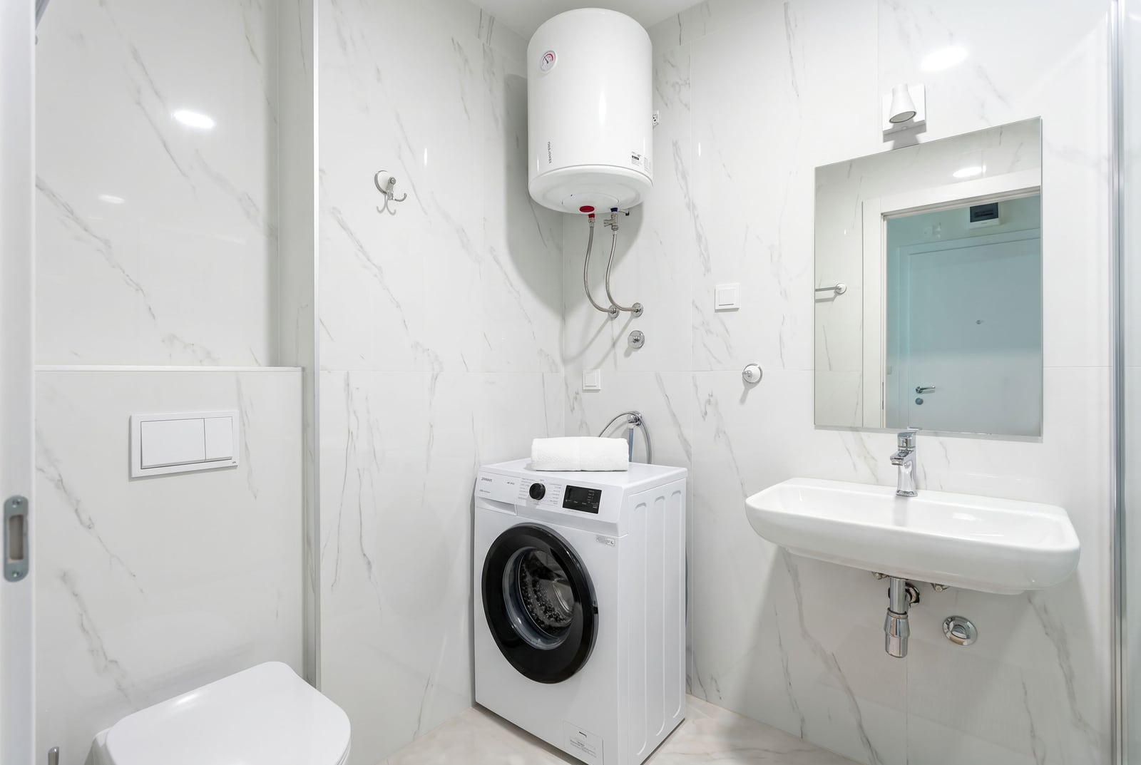 Modern bathroom in an apartment in Bečići, Montenegro: light marble-effect tiles, washing machine, and water heater.