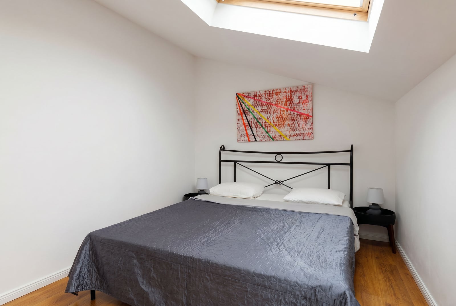 Bedroom in a penthouse in Risan, Montenegro: double bed with a wrought iron headboard and a skylight in the roof.