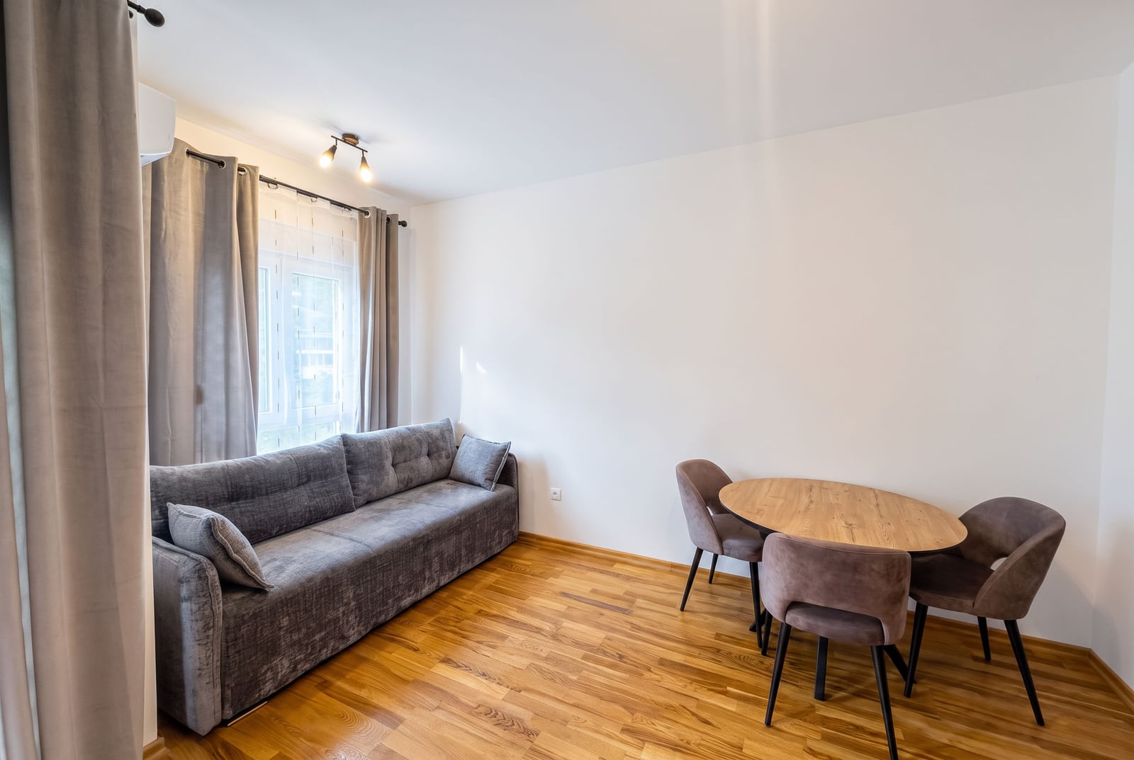 Bright living room in an apartment in Budva, Montenegro: gray sofa, round wooden table and chairs, parquet flooring.