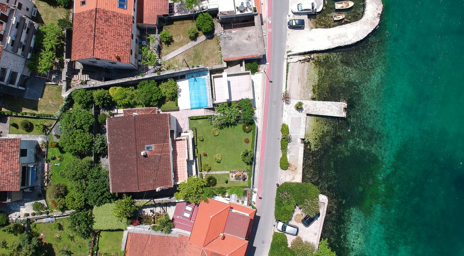Aerial view of a villa in Dobrota, Montenegro: a house with a tiled roof, a green garden, and private access to the sea.