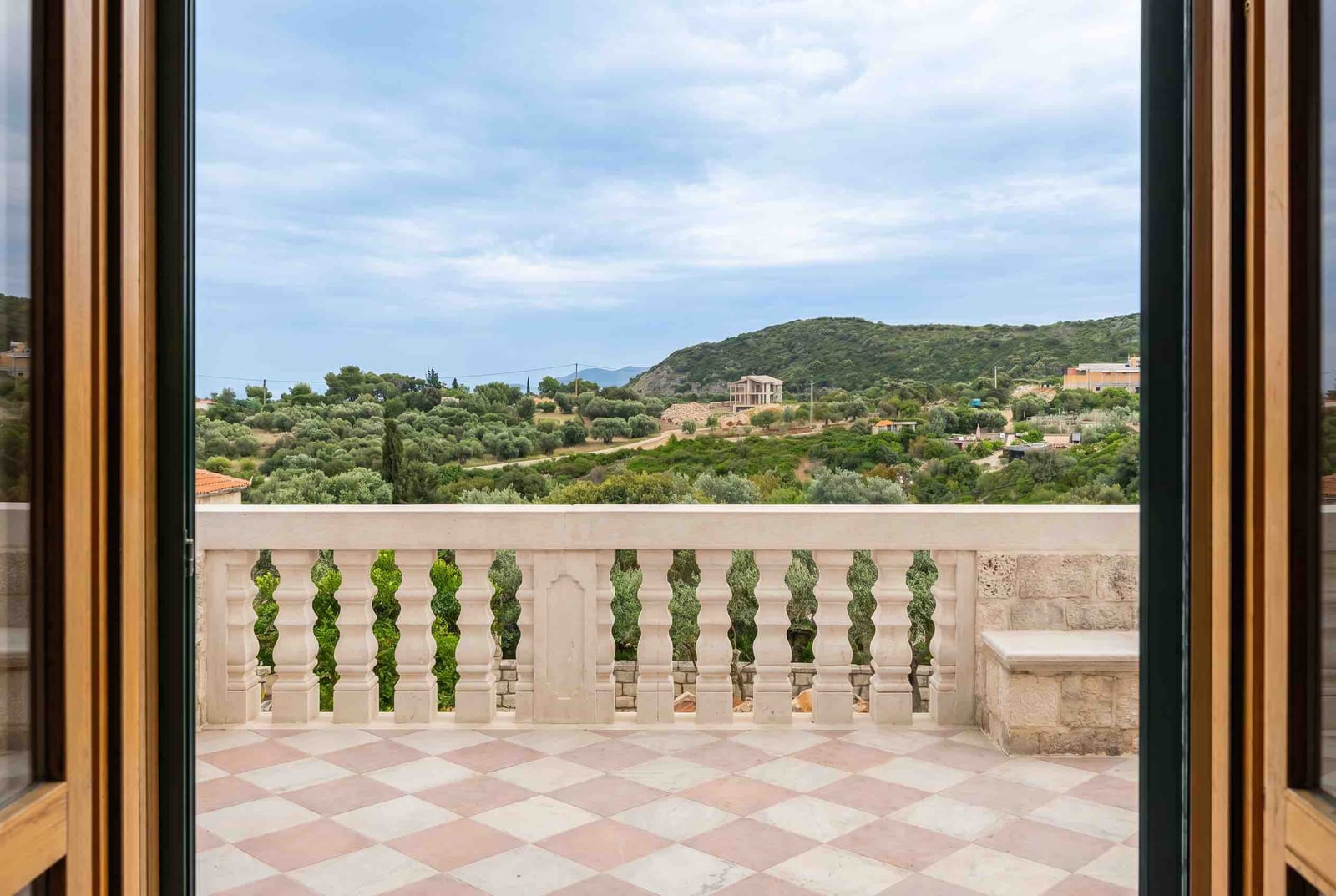 View from a stone balcony over the hills and olive groves in Luštica, Montenegro. Terrace with a balustrade and tiled floor.