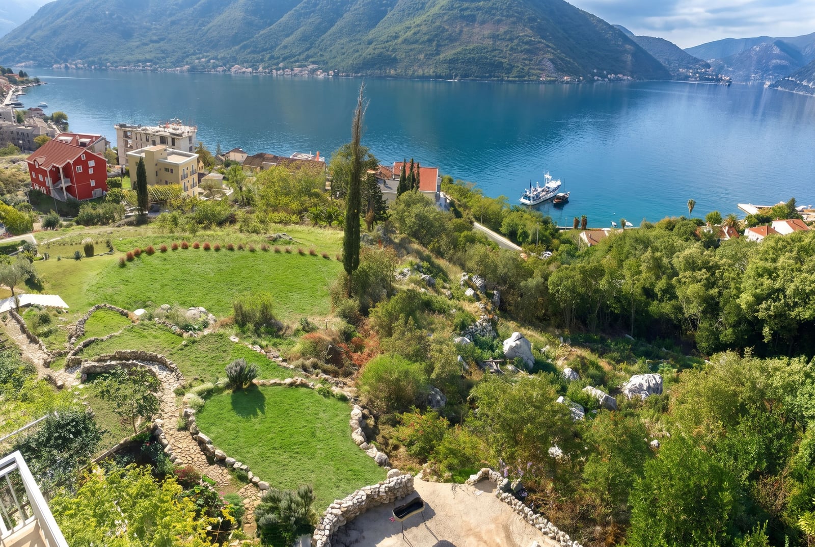 Panoramic view of a bay, mountains, and terraced garden with stone walls and a boat near the shore.