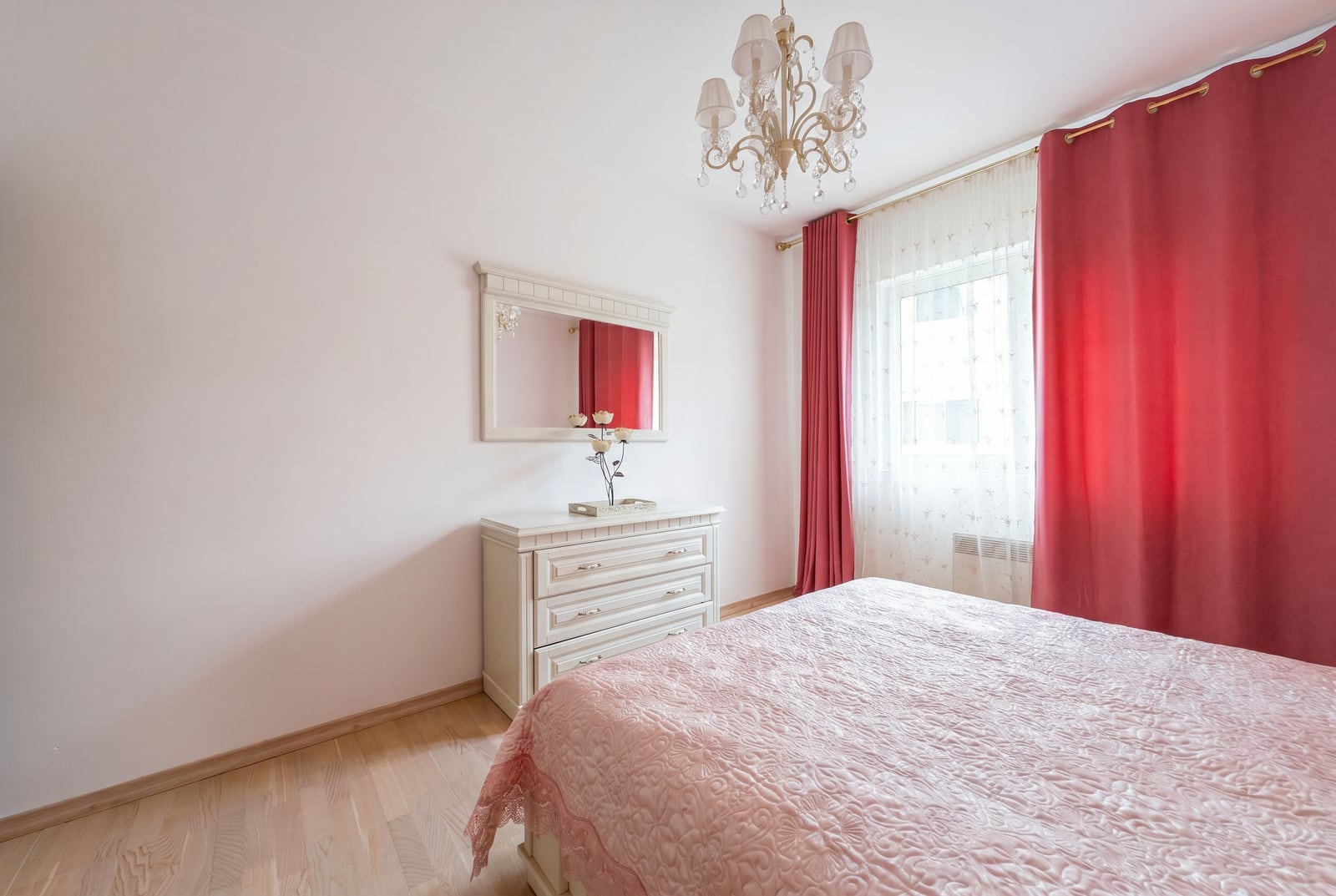 Bright bedroom in an apartment, Kumbor, Montenegro: white furniture, dresser with a mirror, bed, and red curtains.